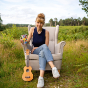 Katie Arnstein sitting in a field with a ukulele