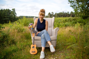 Katie Arnstein sitting in a field with a ukulele